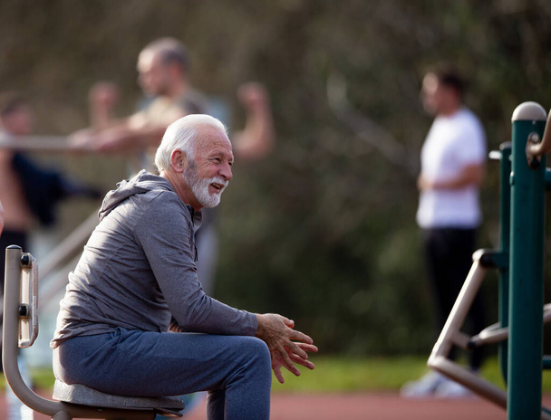 Hombre mayor descansando después de un duro entrenamiento en y gimnasio público al aire libre - Foto, Imagen