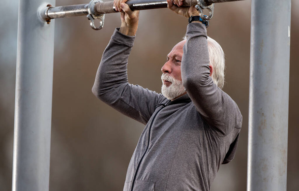 Hombre barbudo mayor en chándal haciendo flexiones en el gimnasio público al aire libre - Foto, imagen