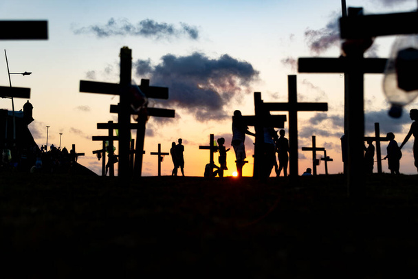 Silhueta de pessoas e cruzes fixadas no chão em honra dos mortos por covid-19. Pôr do sol em Salvador, Bahia, Brasil. - Foto, Imagem
