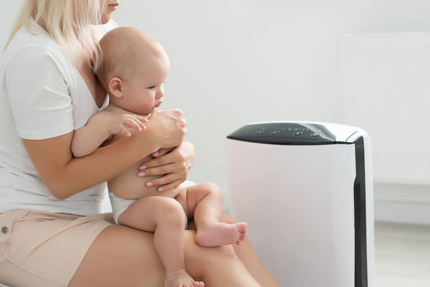 mother and baby near air purifier at home. - Photo, Image