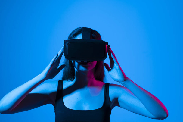 Young attractive curious woman wearing VR goggles and enjoying amazing experience playing and having fun in virtual reality video game. - Foto, Imagem