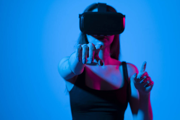 Young woman wearing VR goggles and interacts with cyberspace using swipe and stretching gestures while playing a video game with a friends in metaverse. - Zdjęcie, obraz