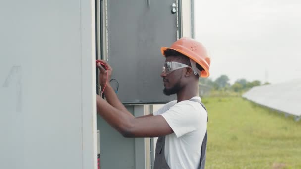 Competent technician in orange helmet and grey overalls standing near switchgear and connection solar station to common network. Production of alternative energy and saving of environment. - Footage, Video