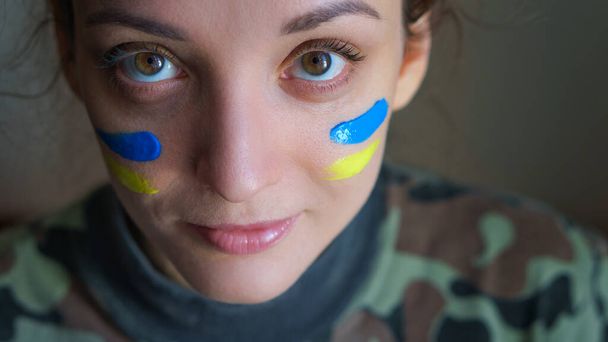 Внутрішній портрет молодої дівчини з синім і жовтим прапором на щоці, одягненої в військову форму, обов'язковий призов в Україні, концепції рівності - Фото, зображення