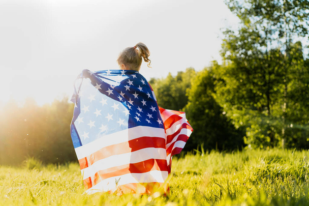beautiful little blonde girl with the American flag in nature in the sunlight - Photo, Image