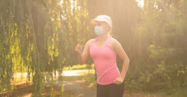 Karantina sırasında formda kalın. Spor yapan genç bir kadın dışarıda koşuyor, yüzünde koruyucu bir maske var. Corona virüsünden ya da Covid-19 'dan tek başına kaçmak. - Fotoğraf, Görsel