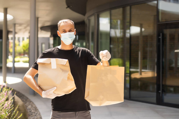 Contactless delivery during COVID-19 pandemic lockdown concept. Courier wearing mask and gloves holds a parcel box and checking address details on the smartphone - Photo, Image