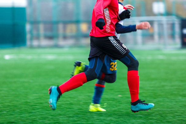 Kırmızı giyimli çocuk sahada futbol oynuyor, top sürüyor. Genç futbolcular yeşil çimlerde top oynuyorlar.. - Fotoğraf, Görsel