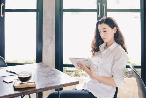Portrait of concentrated young beautiful businesswoman working on tablet and waiting for her customer in cafe. Conceptual of businesswoman lifestyle. - Photo, Image
