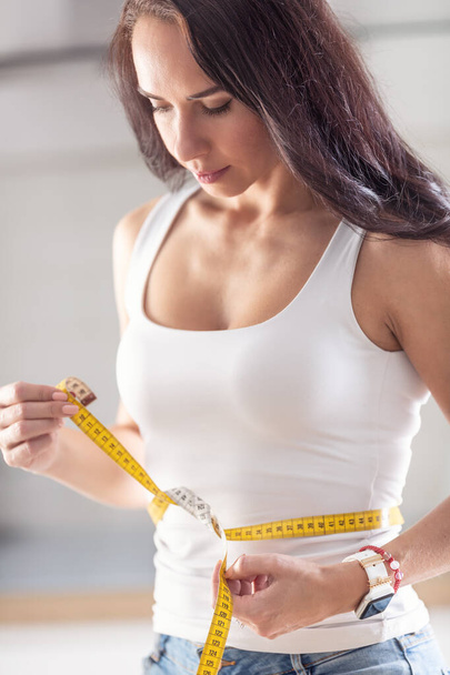 Beautiful fit woman measures how slim her waist is with a tape measure. - Fotó, kép