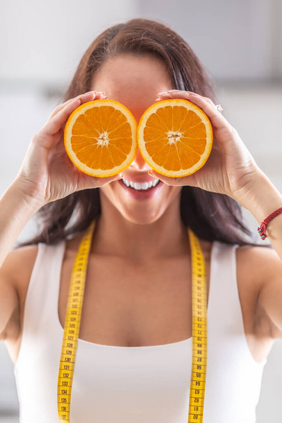 Woman with measuring tape around her neck holds halved orange in front of her eyes. - Foto, Imagem