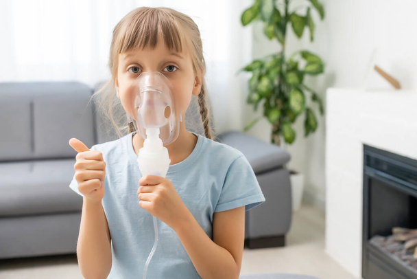 Tyttö tekee inhalaatiota sumuttimella. sairas lapsi pitää inhalaattoria kädessä ja hengittää inhalaattorin kautta kotona - Valokuva, kuva
