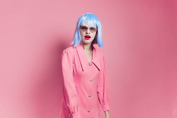 fashionable woman in sunglasses wears a blue wig makeup pink background - Foto, afbeelding