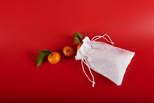 Biała torba z mandarynkami na czerwonym tle - Zdjęcie, obraz
