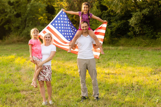 happy family with the flag of america USA at sunset outdoors - Photo, Image