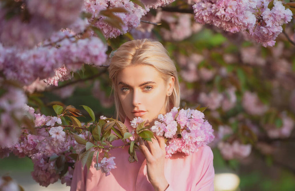 Girl in in blossoms cherry sakura. Outdoor portrait of beautiful sensual fashion girls posing near blooming tree with pink flowers. - Foto, imagen