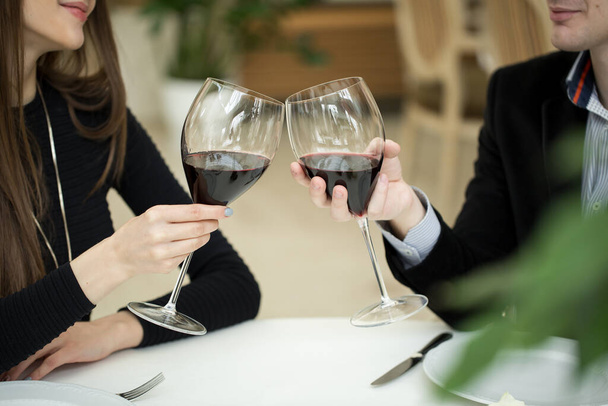 Mooie jonge paar met glazen rode wijn in luxe restaurant. - Foto, afbeelding