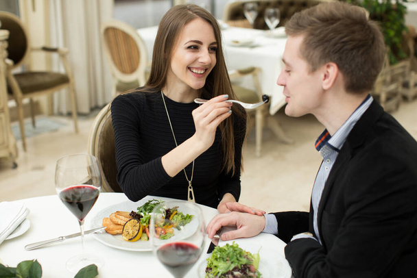 Beautiful young couple feeding each other and smiling while spending time at the restaurant. - Valokuva, kuva