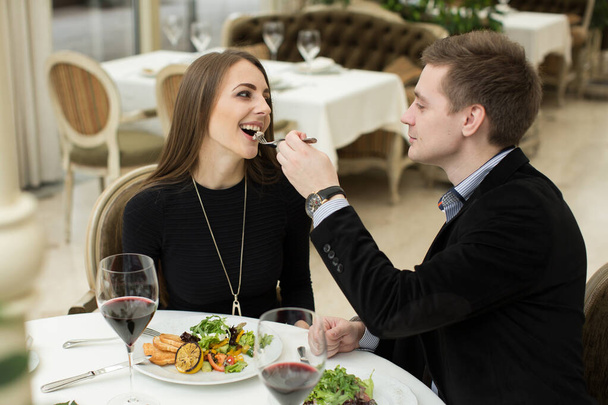 Beautiful young couple feeding each other and smiling while spending time at the restaurant. - Photo, image