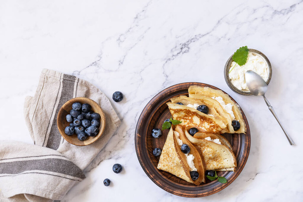 Celebrating Pancake day, healthy breakfast. Delicious homemade crepes with blueberries and riccota on a stone tabletop. Top view flat lay. Copy space. - Photo, Image
