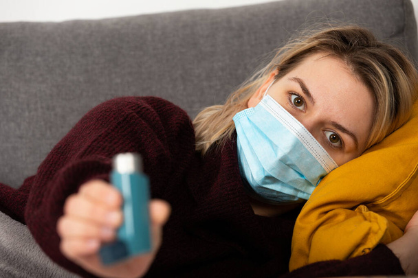 Young woman with coronavirus is having headache and fever, lying on the sofa wrapped in a balnket - Foto, Bild