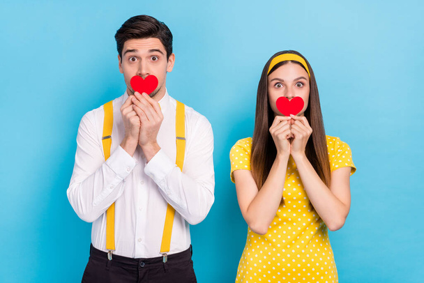 Photo of two funky partners hold small heart paper card covering mouth isolated on blue color background - 写真・画像