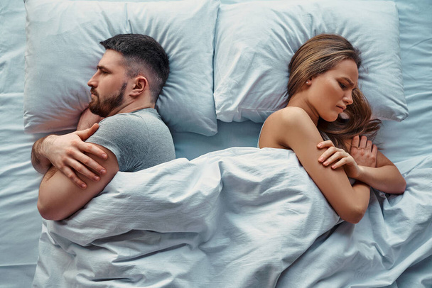 Young beautiful couple lying in bed turned back to back, arms crossed in anger and resentment. Relationship problems.Top view. - Φωτογραφία, εικόνα