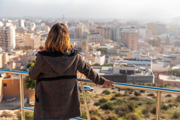 A young tourist girl looking at the city from the viewpoint of Cerro San Cristobal in the city of Almeria, Andalucia. Spain. Costa del sol in the mediterranean sea - Фото, изображение