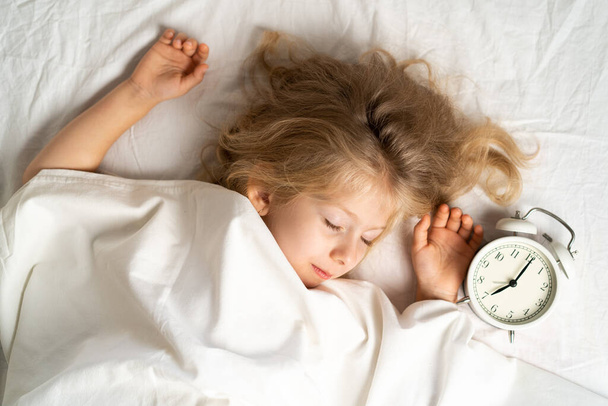 Маленькая блондинка сладко спит в кровати с белым нижним бельем. место для текста. здоровый сон ребенка - Фото, изображение