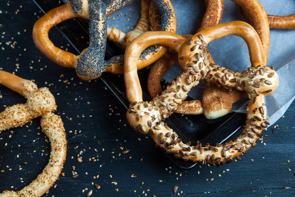Fresh prepared homemade soft pretzels. Different types of baked bagels with seeds on a black background. - Foto, Imagem
