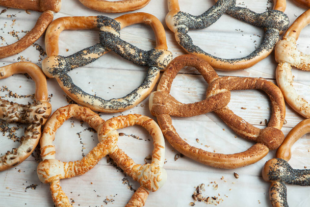 Fresh prepared homemade soft pretzels. Different types of baked bagels with seeds on a black background - Zdjęcie, obraz
