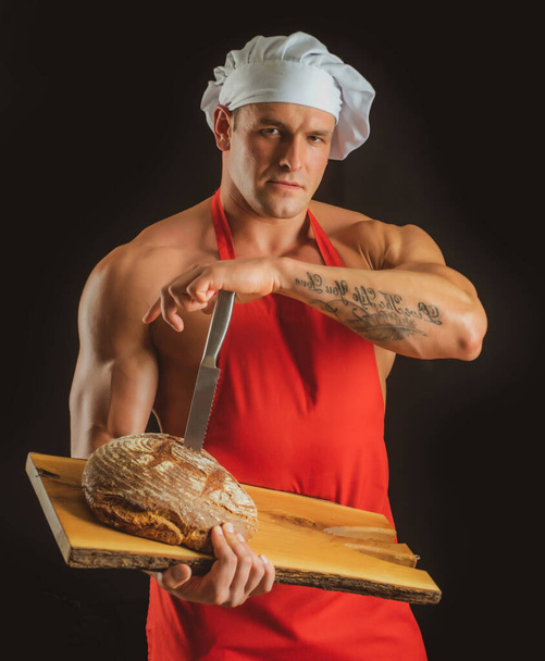 Cooking and baking. Chef baker man in apron. Sexy guy with bread and knife. - Zdjęcie, obraz