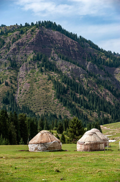 Dwie kirgiskie jurty na trawie w środku gór. Jurty są tradycyjne budynki narodowe lokalnych mieszkańców, ala-kul jezioro Terskey Alatau pasmo górskie, Kirgistan, Azja Środkowa. - Zdjęcie, obraz