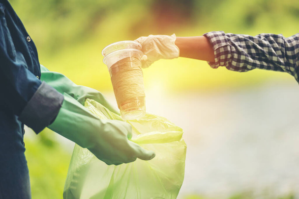 Human hand picking up plastic glass into green bin bag on park, charity volunteer concept - Fotografie, Obrázek