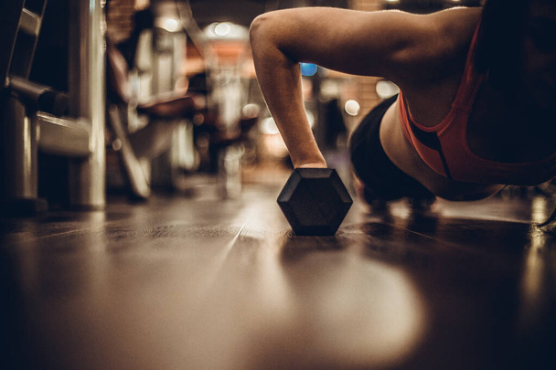 Fitt nő fiatal során push ups edzés az edzőteremben súlyzók. - Fotó, kép