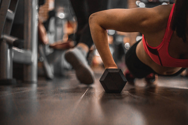 Fit woman young doing push ups exercise with dumbbells in the gym. - Photo, Image