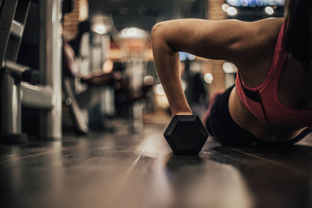 Fit woman young doing push ups exercise with dumbbells in the gym. - Photo, Image