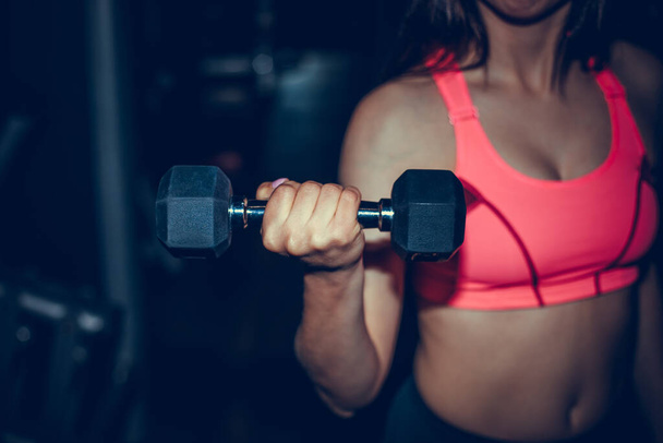 Fitness sporty woman in training pumping up muscles with dumbbells. Young sports sexy fitness woman body with dumbbells posing on dark background. - Foto, Imagem