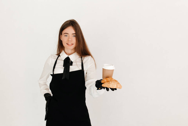 Jonge serveerster serveert haar klanten met vers gebakken croissants en een afhaalkoffie. Perfect ontbijtconcept - Foto, afbeelding