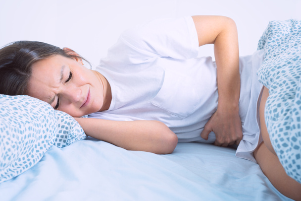 月経痛、胃の痛みや腹部の痛みに苦しむベッドの女性。月経期間又はPMS - 写真・画像