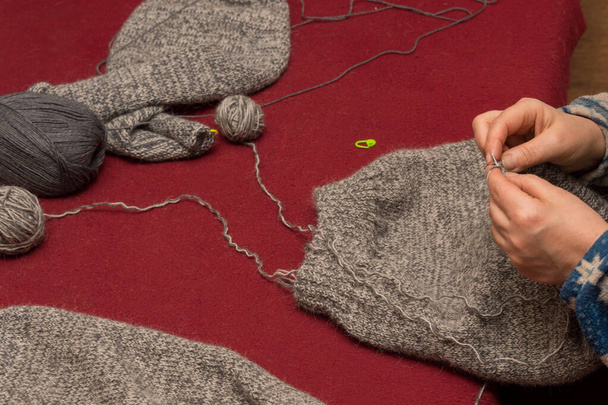 女性の手は、それの横にある毛糸の針でセーターを編んでいるウールのボールです。背景はバーガンディ。. - 写真・画像