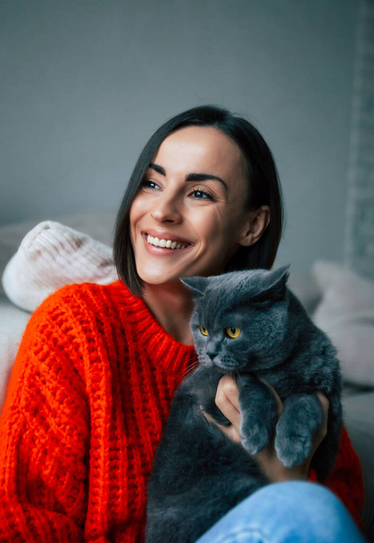 Close up portrait of happy gorgeous young brunette woman holding and hugging her cute British shorthair cat at home - 写真・画像
