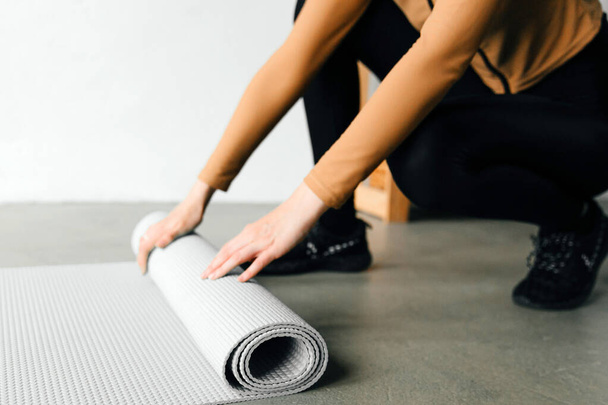 Young woman's hands rolling her grey mat after a yoga class - Foto, imagen