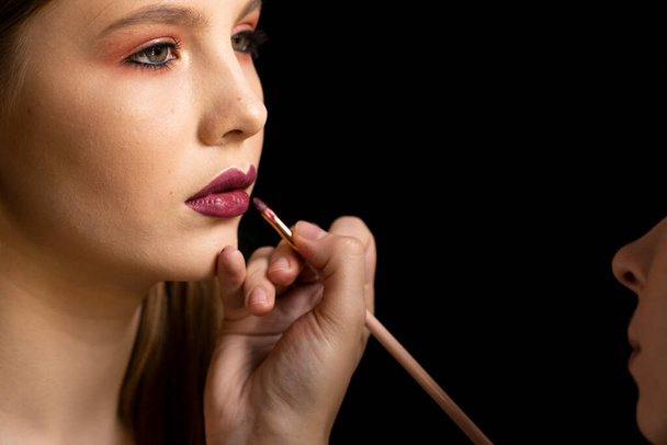 Make-up artist apply red lipstick. Part of attractive womans face with fashion red lips makeup. - 写真・画像