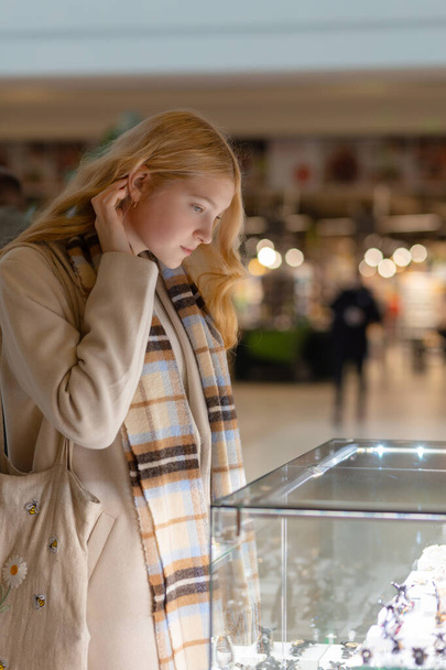 junge Frau, die sich die Schaufenster und den Schmuck ansieht, um sie sich näher anzusehen, schöne Studentin, blondes Modemodel im Juwelier-Einkaufszentrum - Foto, Bild