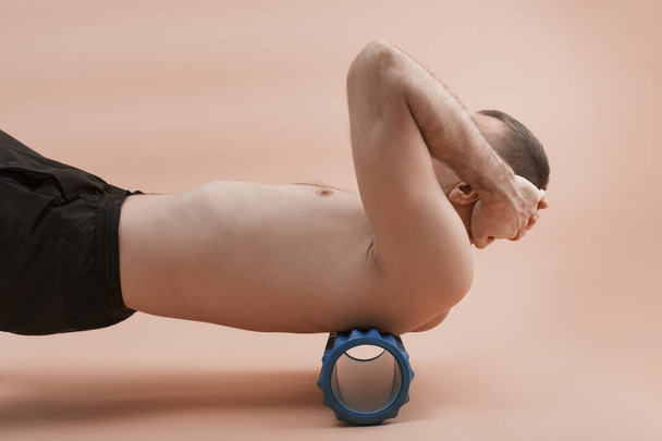 Αθλητικός άνθρωπος που χρησιμοποιεί myofascial ρολό για τους μυς και την περιτονία τεντώνεται πίσω. Όμορφος άνθρωπος κάνει ασκήσεις με ρολό αφρού. Πλευρική άποψη. - Φωτογραφία, εικόνα