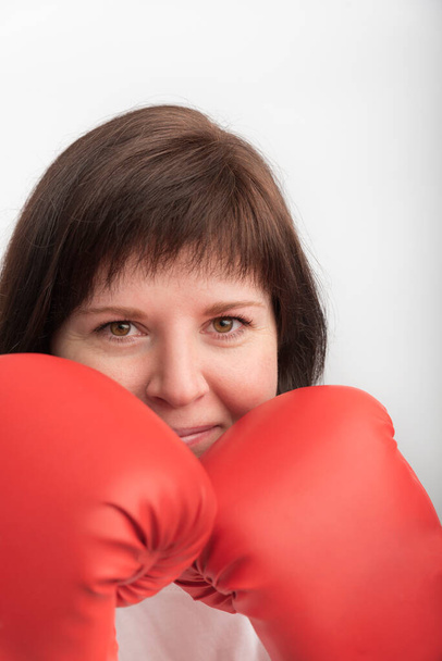 Close-up portrait of young dark-haired woman in red wrestling gloves. Woman boxer. Vertical frame. White background. - Photo, Image
