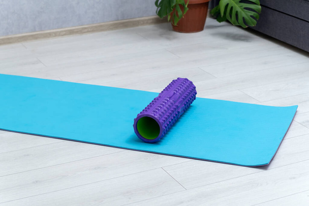 Foam roller for self-massage on blue yoga mat. Equipment for myofascial release. Massage roller. Workout at home - Photo, Image