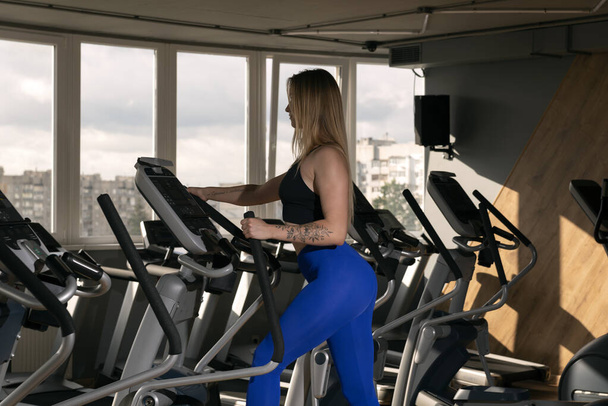 Jeune femme mince avec une belle silhouette est engagée dans la salle de gym sur un entraîneur elliptique. Cardio-training - Photo, image
