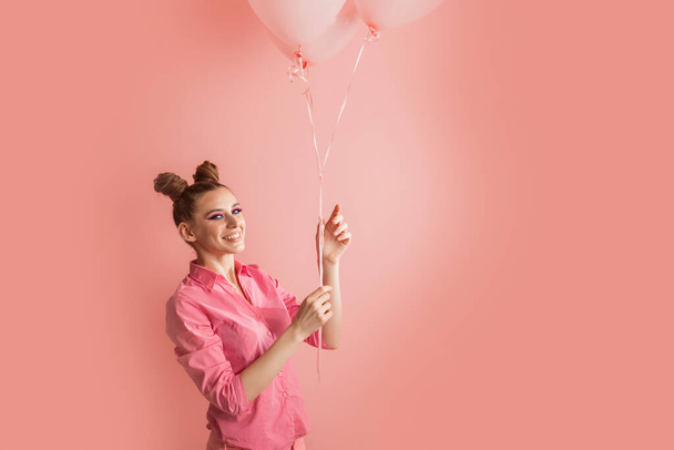 Muotokuva erittäin onnellinen tyttö ilmapalloja käsissään. Iloisen nuori nainen ruusuisessa paidassa vaaleanpunaisella taustalla - Valokuva, kuva